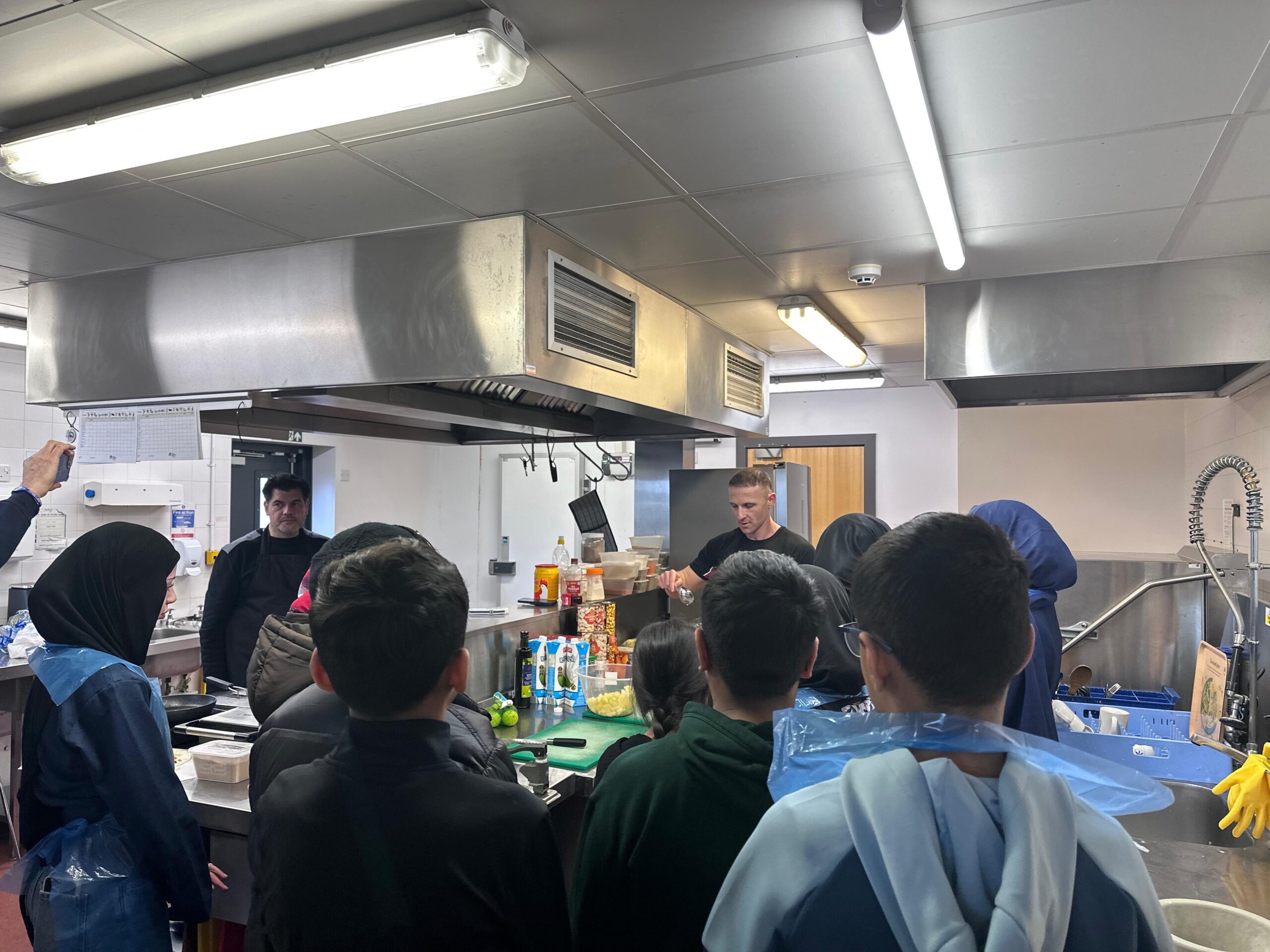 Young people gather around a cookery demonstration in the Chai Centre kitchen.